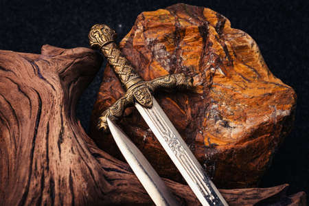 Knight's sword on the background of an old textured wooden driftwood and a rough stone of brown colorの写真素材