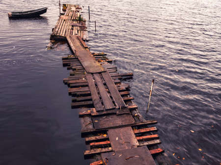 View of the river with a lonely fishing boat moored to an old wooden pier. Vintage style. Russia,...