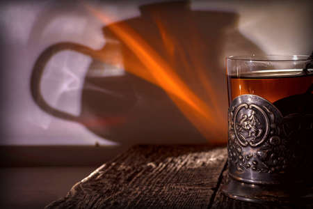 Tea in an old glass-holder made of dark metal with stamped floral ornaments and an image of a rider on a horse on a textured wooden table.の写真素材