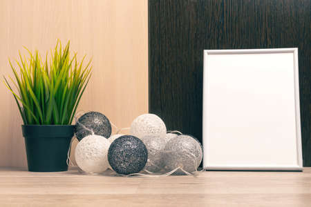 White frame with place for text and a green plant in a black pot against the background of a black and white wall and decorative balls. Stylish room interior.の写真素材