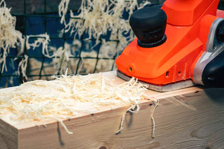 Background with an orange electric plane on the processed surface of a wooden beam. Woodworking...
