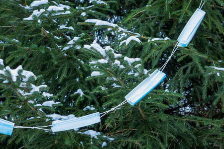 A garland of medical masks decorates the spruce trees with snow. New year and christmas concept amid...