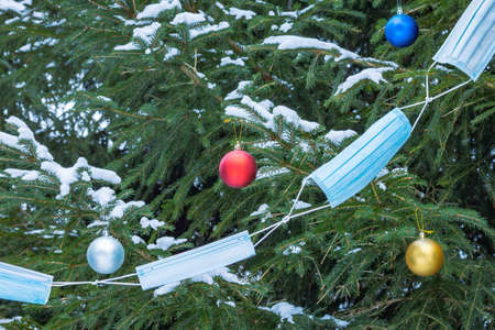 A garland of medical masks and multicolored festive balloons on fir trees with snow. New year and...