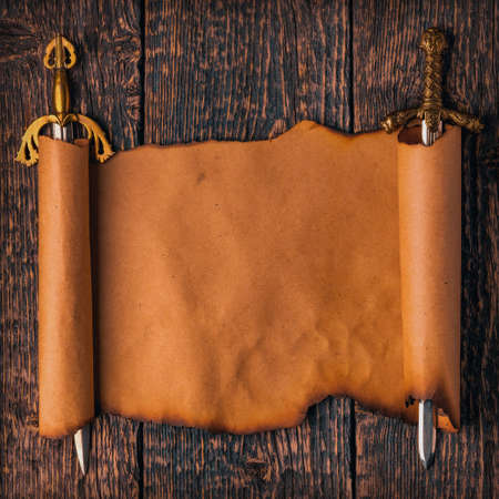 Scroll of old paper with burnt edges stretched on the blades of knight swords against the background...