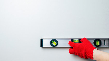 A worker's hands in red protective gloves hold a metal spirit level against a white wall. Home master conceptの写真素材