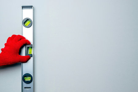 A worker's hands in red protective gloves hold a metal spirit level against a white wall. Home master conceptの写真素材