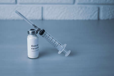 Ampoule of vaccine with the inscription COVID-19 and a syringe for injection on a gray background....