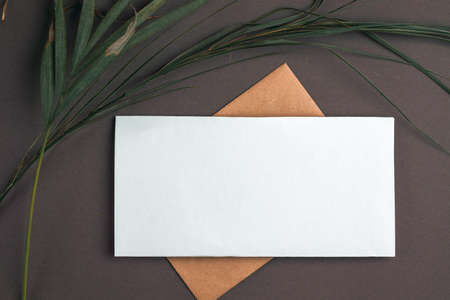 Blank white sheet and vintage envelope mockup on gray background with dry palm leaves. Flat lay, top view.の写真素材