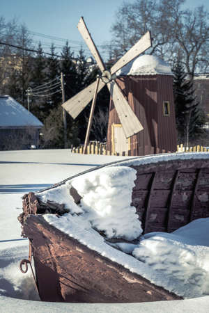 Old fishing wooden boat covered with snow on the background of the mill.の写真素材