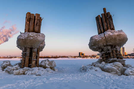 Wooden pillars with blocks of ice stick out from under the ice of a frozen river against the backdrop of a blue sky at sunset.の写真素材