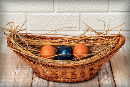 Easter eggs on straw in a wicker basket on an old wooden table surface. Easter celebration concept. Flat layの写真素材