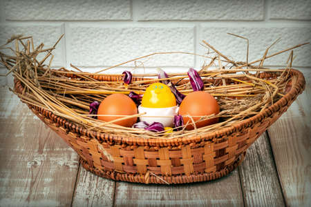 Easter eggs on straw in a wicker basket on an old wooden table surface. Easter celebration concept. Flat layの写真素材