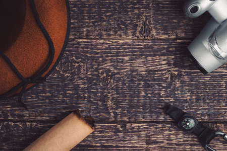 A wide-brimmed hat, a camera, a compass and a scroll of paper on an old brown wooden surface. Travel and adventure conceptの写真素材