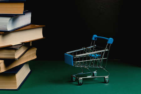 A stack of books and a grocery cart on a green background. Bookstore, sales conceptの写真素材