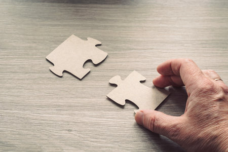 Close-up of a man's hand connecting a puzzle on a wooden surface. Business solutions, success and strategy conceptの写真素材