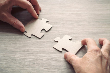 Close-up of a man's hand connecting a puzzle on a wooden surface. Business solutions, success and strategy conceptの写真素材