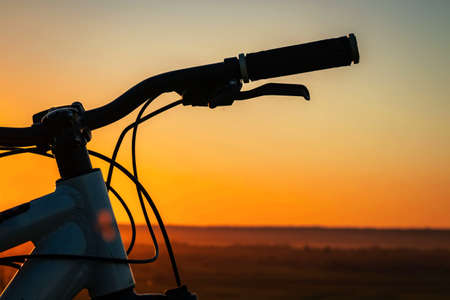 Silhouette of a bicycle against the background of a sunset with an orange sky.の写真素材