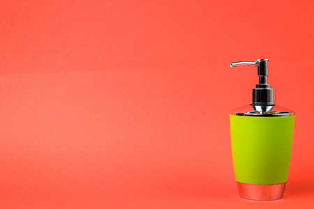 Dispenser of green color for liquid soap isolated on orange background. Close-up.の写真素材