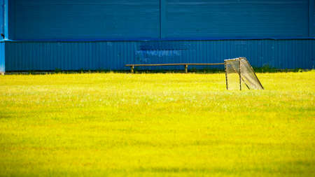 View of a soccer field made of yellow grass with a goal against a blue wooden wall. Sports conceptの写真素材