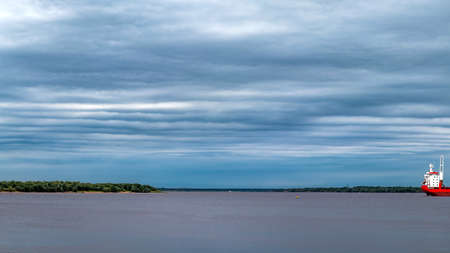 Cloudy sky above the water surface of a large river. Marine vessel in the roads. Northern Dvina, Arkhangelsk, Russiaの写真素材