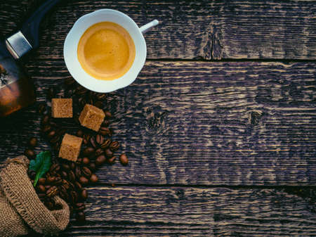 Cezve, a cup of coffee, a bag of spilled coffee beans and cane sugar lumps on an old wooden surface....
