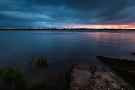 Beautiful view of the river with the effect of blurred water reflecting cloudy gray sky at sunset.の写真素材