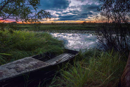 Beautiful evening sunset with sky reflection on the surface of the lake with an old wooden boat on the shore.の写真素材