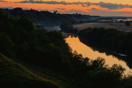 Nice view of the river among the trees reflecting the orange sky at sunset.の写真素材