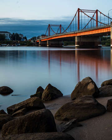 Orange City Bridge across the river. View from the shore with stones in the foreground.