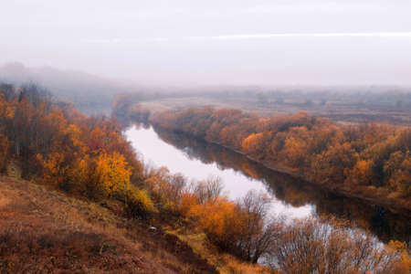 View from the hill to the river with autumn trees along the banks. Foggy morningの写真素材