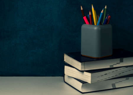 A stack of books and a gray stationery glass with multi-colored pencils on the table. Back to school conceptの写真素材