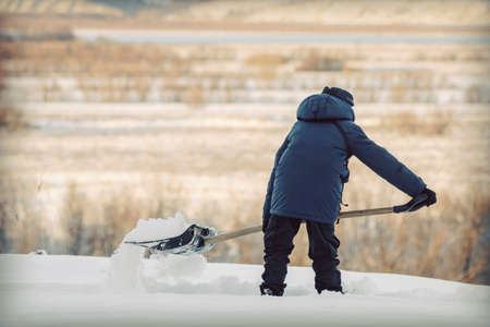 A teenager with a snow shovel cleans a path among snowdrifts on the background of nature.の写真素材