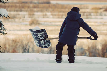 A teenager with a snow shovel cleans a path among snowdrifts on the background of nature.の写真素材