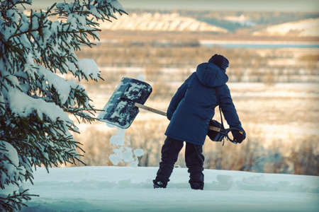 A teenager with a snow shovel cleans a path among snowdrifts on the background of nature.の写真素材