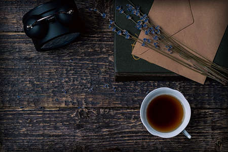 A cup of coffee, an alarm clock, a sprig of dried lavender and a book on the background of the texture of the old wood.の写真素材