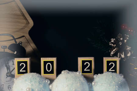 Numbers 2022 on wooden planks, black retro alarm clock and Christmas decorations on dark background...