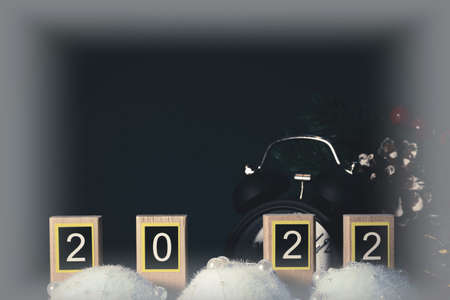 Numbers 2022 on wooden planks, black retro alarm clock and Christmas decorations on dark background with creative vignetting. New Year holidays concept.の写真素材