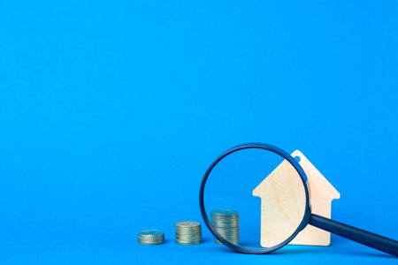 Wooden house keychain, magnifier and stacks of coins on a blue background.の写真素材