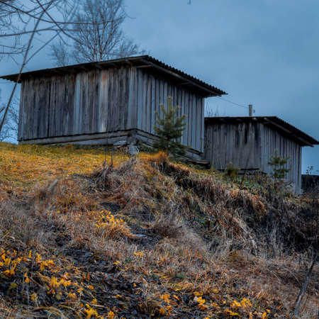 Old wooden buildings on top of a hill with yellowing autumn grass.の写真素材