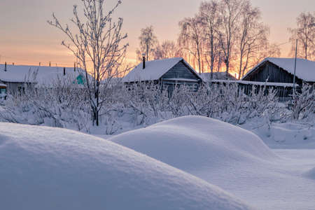Beautiful winter view of the outskirts of the village at sunset. Rocks covered with snow in the foregroundの写真素材