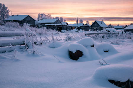 Beautiful winter view of the outskirts of the village at sunset. Rocks covered with snow in the foregroundの写真素材