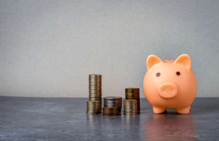 Pink piggy bank and stacks of coins on a gray marble surface.の写真素材