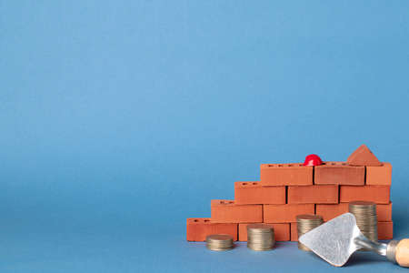 Stacks of coins in the form of steps against a background of red brickwork and a masonry trowel.の写真素材
