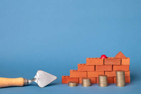 Stacks of coins in the form of steps against a background of red brickwork and a masonry trowel.の写真素材