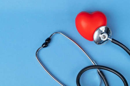 Stethoscope and rubber red heart on a blue background with space for text. Heart health, healthcare concept. Flat layの写真素材