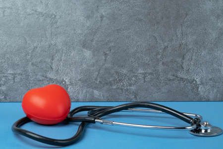 A stethoscope and a rubber red heart on a blue table against a gray marble wall.の写真素材