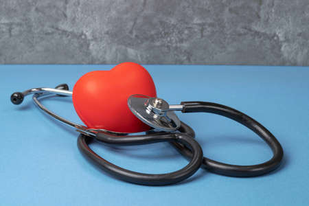 A stethoscope and a rubber red heart on a blue table against a gray marble wall.の写真素材