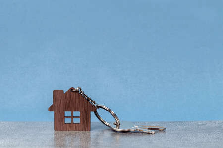 Wooden house and keys on a metal chain against a gray wall. New home buying conceptの写真素材