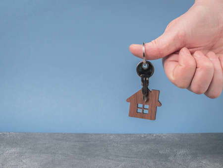 Keys with a model of a wooden house in a man's hand close-up. Home buying concept. Copy spaceの写真素材