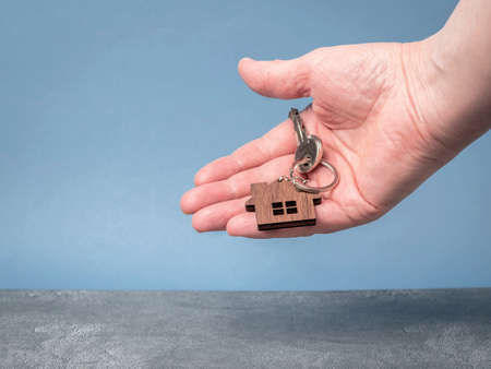 Keys with a model of a wooden house in a man's hand close-up. Home buying concept. Copy spaceの写真素材